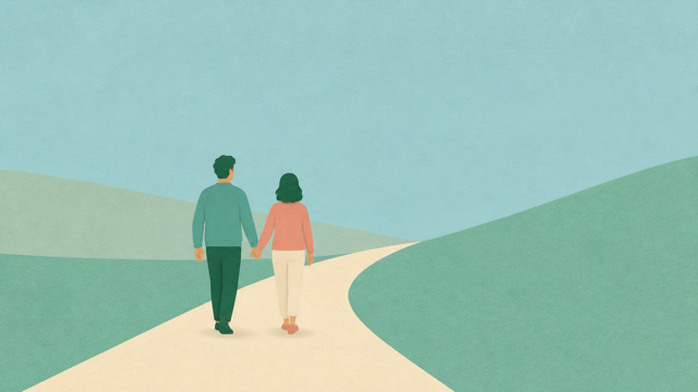 Two people walking together along a green path toward distant hills.