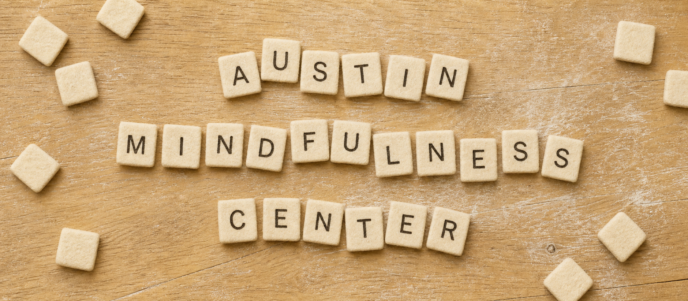 Cream felt letter tiles spelling Austin Mindfulness Center on a warm, textured wooden table.